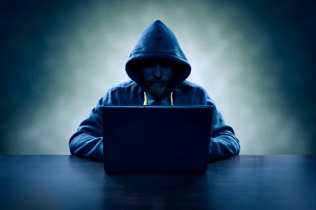 Hooded computer hacker stealing information with laptop