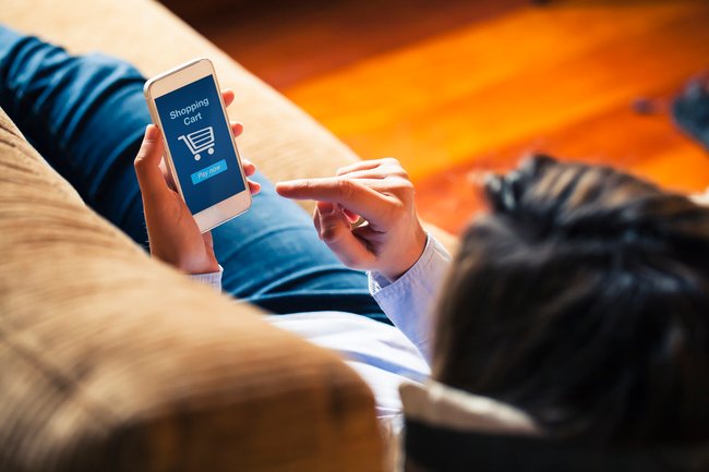 Woman shopping by mobile phone laying at home. Blue screen.