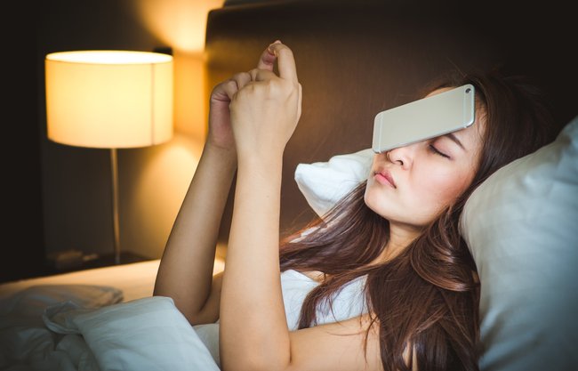 Sleepy asian woman in white bed, dropped smart phone on face