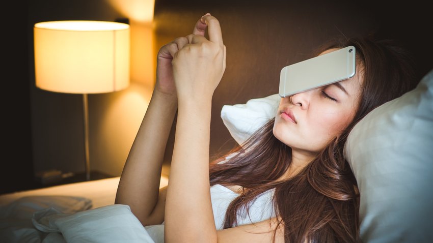 Sleepy asian woman in white bed, dropped smart phone on face