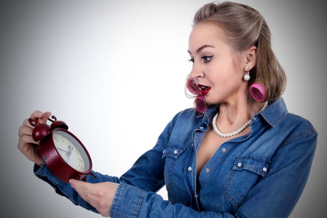 Frightened young woman in curlers with alarm clock