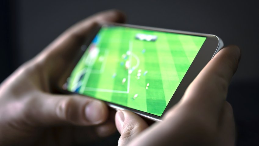 Watching football and sport stream with mobile phone. Man streaming soccer game live, video replay or highlights online with smart device. Sports fan and program of tv network in smartphone screen. (Watching football and sport stream with mobile phone