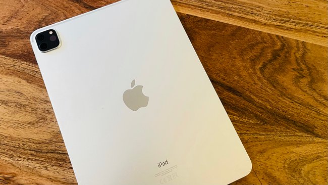 Auf einem Holztisch liegt ein hellgraues iPad mit der Rückseite nach oben.