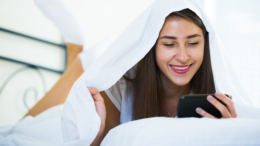 Frau versteckt sich mit Handy unter Decke