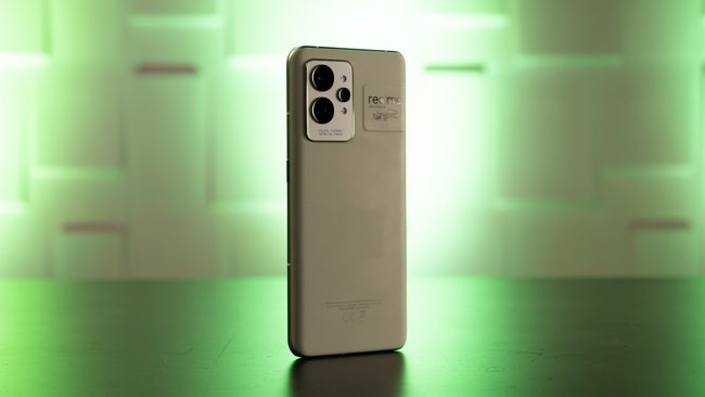 The Realme GT 2 Pro smartphone is standing on a table with the back facing the camera.  It is illuminated with green light.
