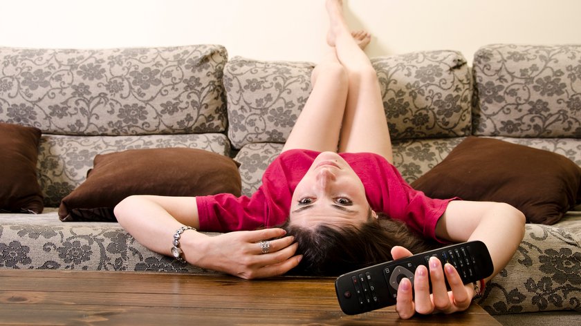 Frau liegt kopfüber auf dem Sofa und schaut Fernsehen