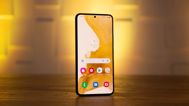 Auf einem Tisch steht das Smartphone Samsung Galaxy S22 und wird von gelbem Licht angestrahlt.