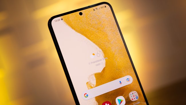 Im Vordergrund ist das Smartphone Samsung Galaxy S22 mit aktiviertem Display, der Hintergrund ist orange beleuchtet.