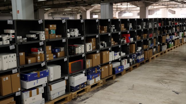Eine Regalreihe im rebuy-Warenlager. Verpackte Konsolen, Laptops und Smartphones werden hier gelagert.