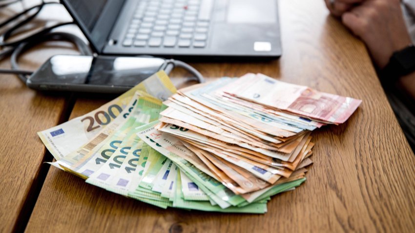 Geldschein im Wert von mehreren Tausend Euro liegen auf einem Tisch, daneben ein Laptop.