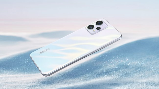 The silver smartphone Realme 9 lies on white sand.