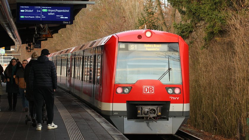 Eine einfahrende S.Bahn in Hamburg. Am Bahngleis stehen Menschen.