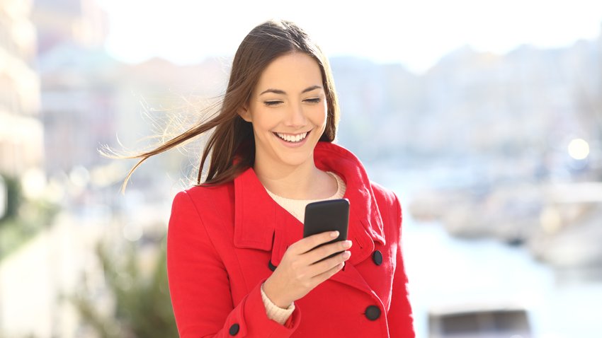 Eine Person in einem roten Mantel schaut lächelnd auf das Smartphone.