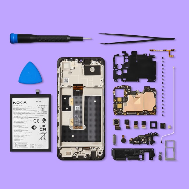 Auf einem violetten Tisch liegt das geöffnete und auseinander gebaute Smartphone Nokia G22 mit Werkzeug von iFixit.