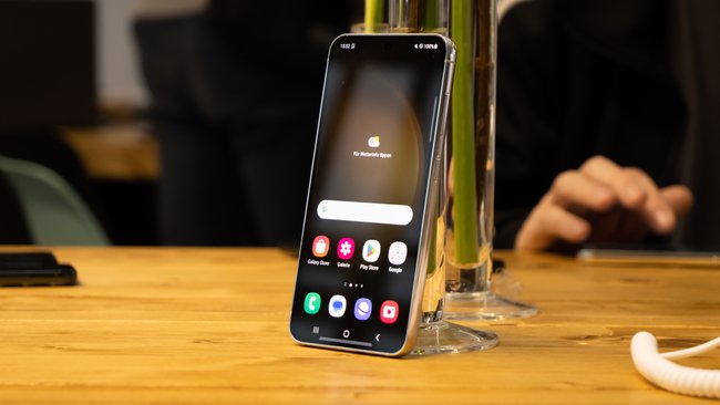Auf einem Tisch lehnt das Smartphone Samsung Galaxy S23 an einer Vase.