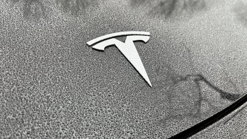 Das silberfarbene Logo des Autoherstellers Tesla auf einer nassen Motorhaube.