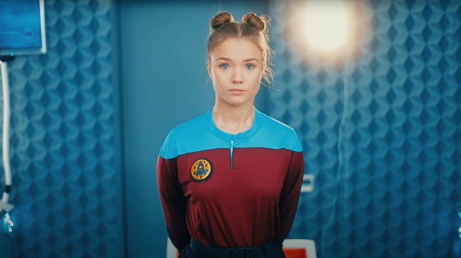 Die YouTuberin Julia Beautx steht in einem blauroten Uniform vor einer blauen Wand.