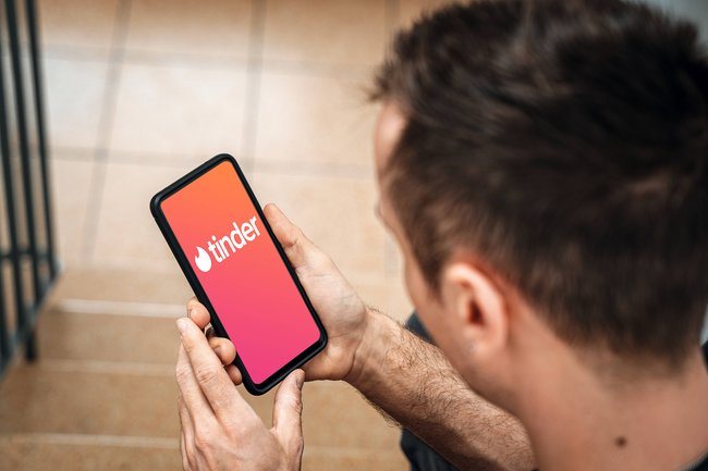 Ein Mann hält ein Smartphone in der Hand, das die App Tinder anzeigt.