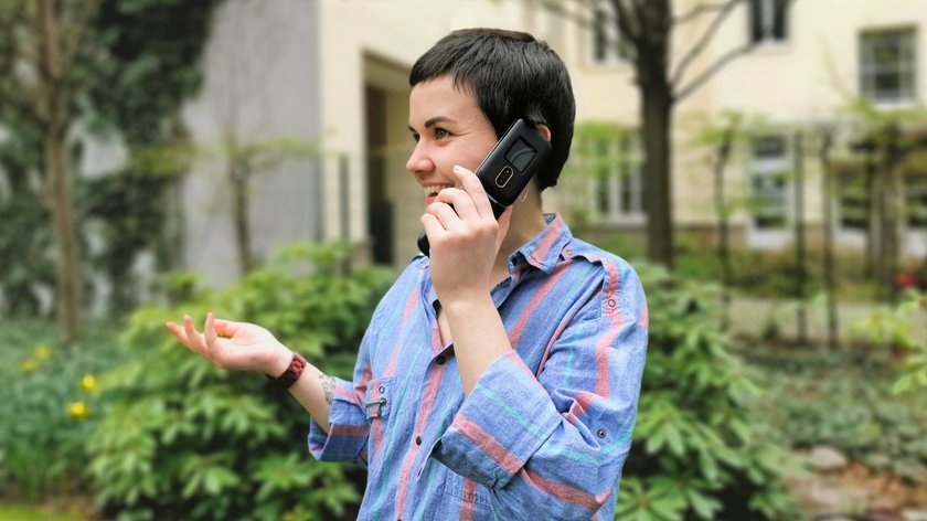 Eine Frau telefoniert über ein Seniorenhandy, im Hintergrund ist ein Garten.