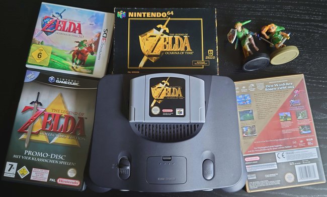 Ein Nintendo 64 mit verschiedenen Spieleausführungen zu "The Legend of Zelda: Ocarina of Time". Rechts oben sind zwei Figuren von Link.