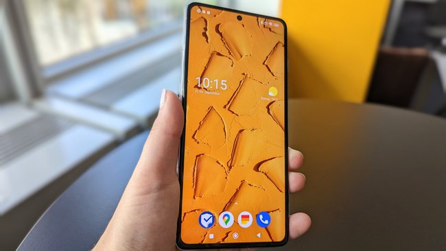 Eine Hand hält das Smartphone Poco F4 GT. Das Display ist aktiviert und zeigt einen orangen Hintergrund.