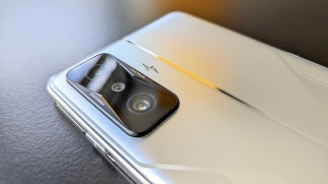 Auf einem schwarzen Tisch liegt das Smartphone Poco F4 GT mit der silbernen Rückseite nach oben. Das Dreifach-Kameramodul ist sichtbar.