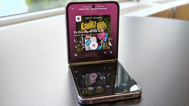 Auf einem schwarzen Tisch liegt das Samsung Galaxy Z Flip4. Es läuft der Podcast "Kaulitz Hills".