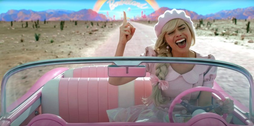 Margot Robbie sitzt als Barbie im pinken Auto und singt ein Lied mit.