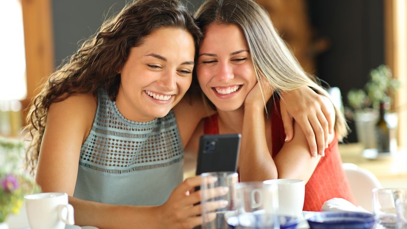 Zwei Frauen sitzen nebeneinander und schauen ins Handy.