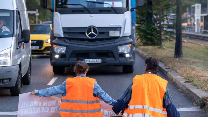 Vor einem LKW sitzen Klimaaktivistend er Letzten Generation auf der Straße.