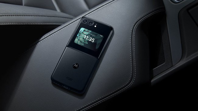 Auf einem schwarzen Autositz liegt das aufgeklappte Handy von Motorola.