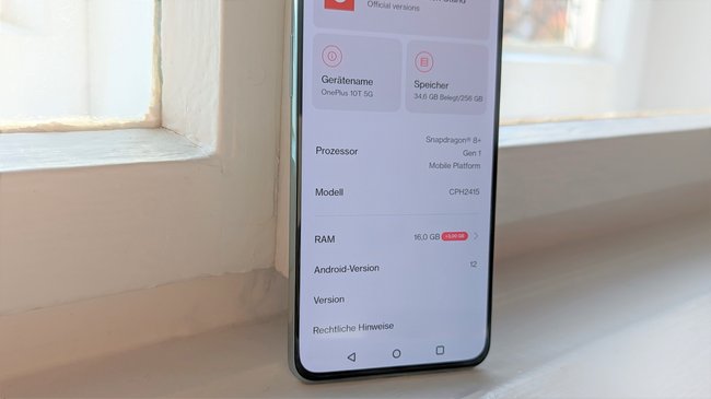 Auf einem Fensterbrett steht das Smartphone OnePlus 10T. Auf dem geöffneten Display werden die Geräteinformationen angezeigt.