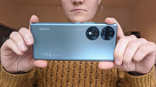 Eine Frau hält die Rückseite des Honor 70 in die Kamera und nimmt ein Foto auf.