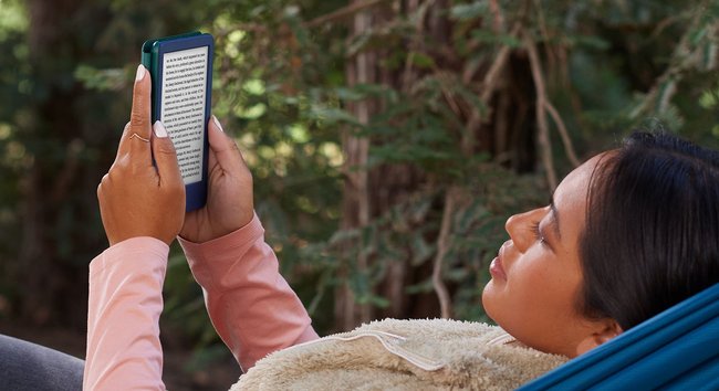 Eine weiblich gelesene Person liegt in einer Hängematte und liest in dem E‑Book-Reader Kindle.
